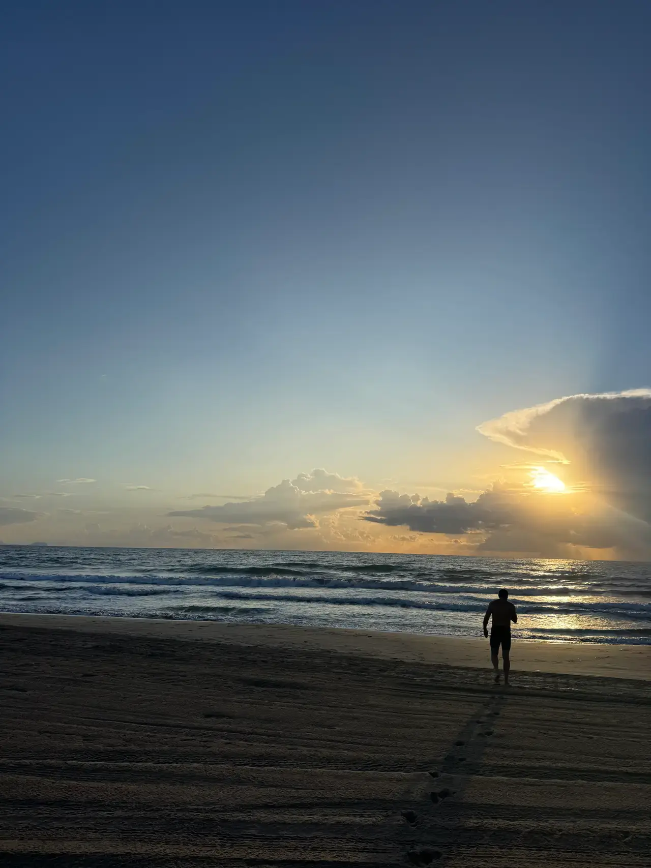 A swimmer walking into the sea at sunrise