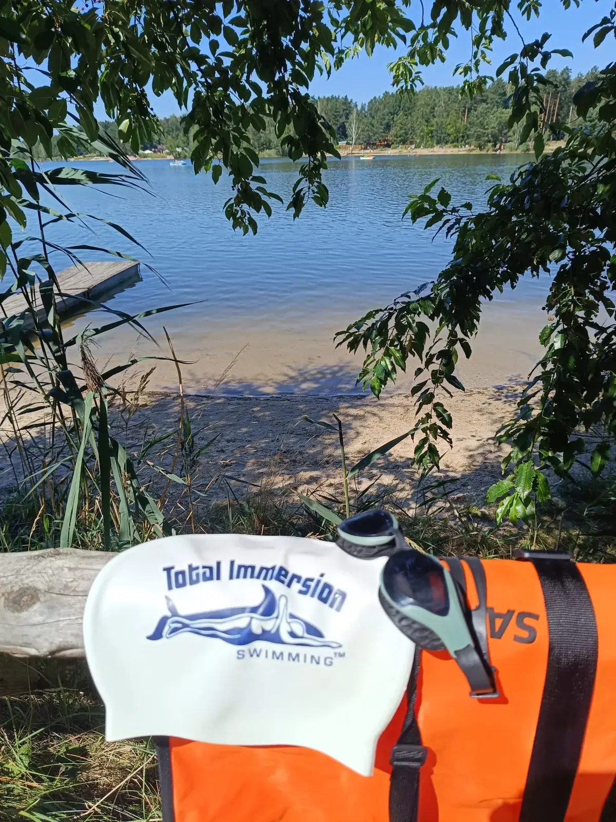 A swim cap and goggles resting on an orange tow float by the lake