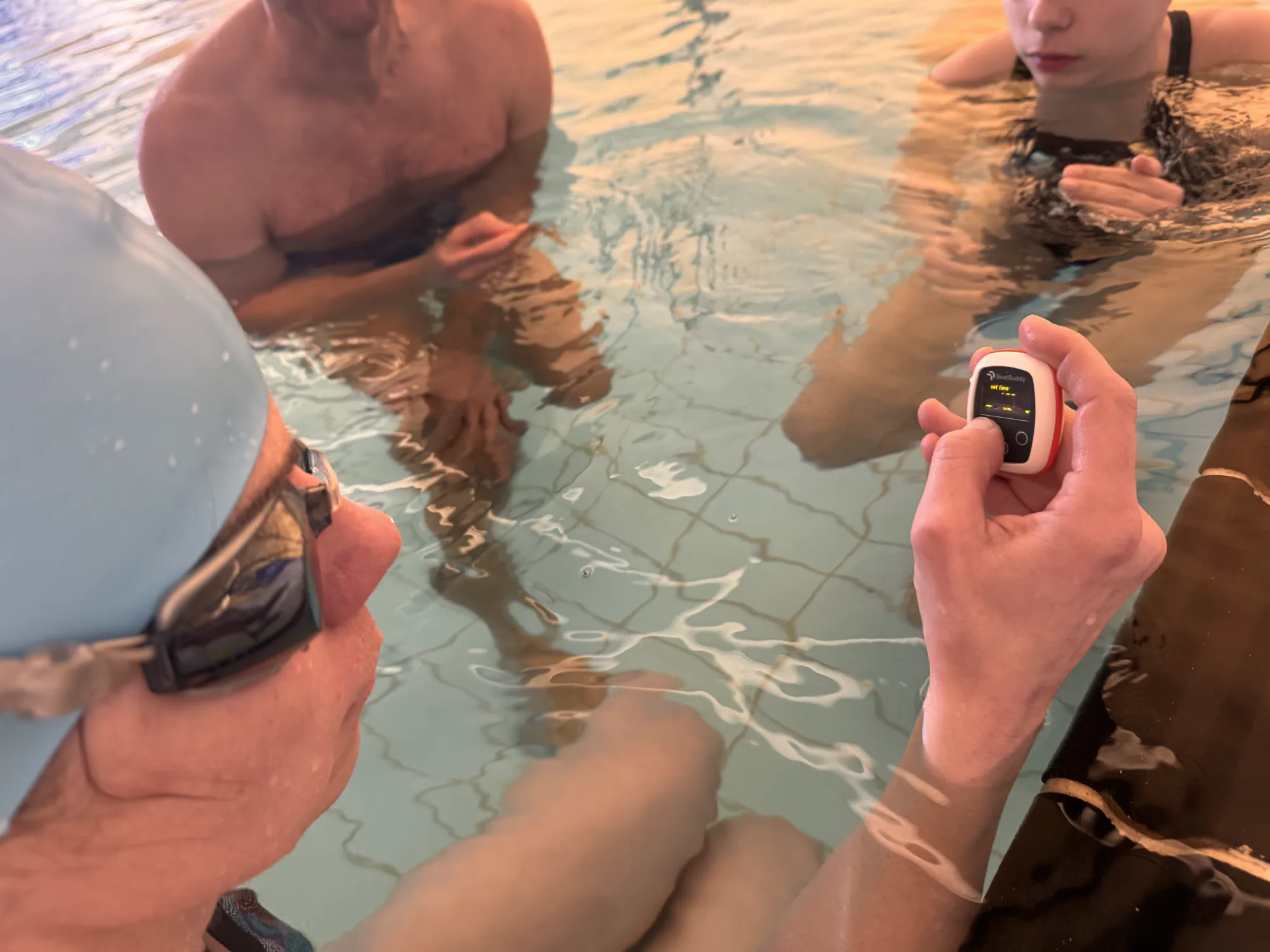 Swimmers standing in the shallow end while one sets a Vimo device