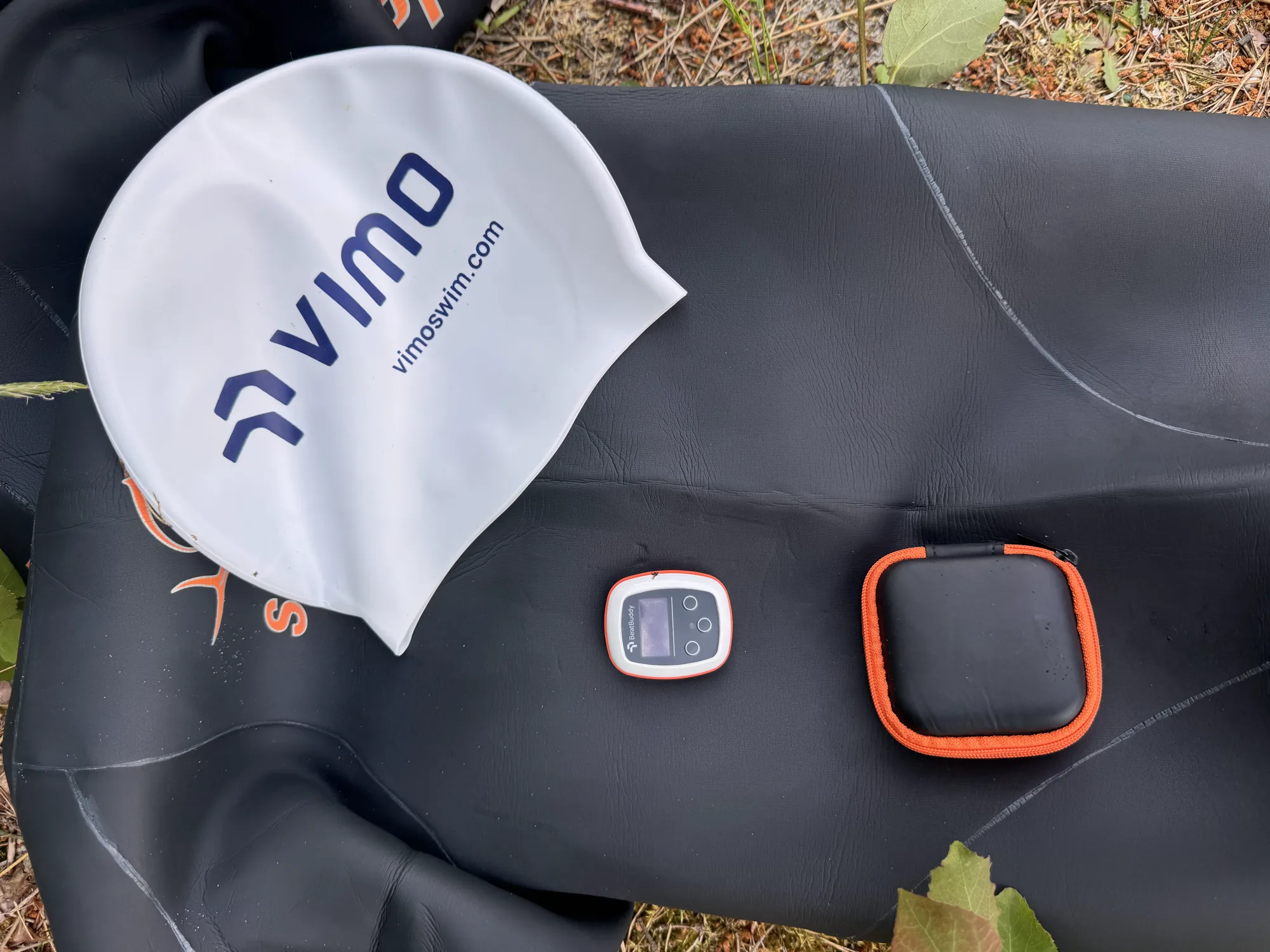 Vimo swim cap, device and case laid out on a wetsuit