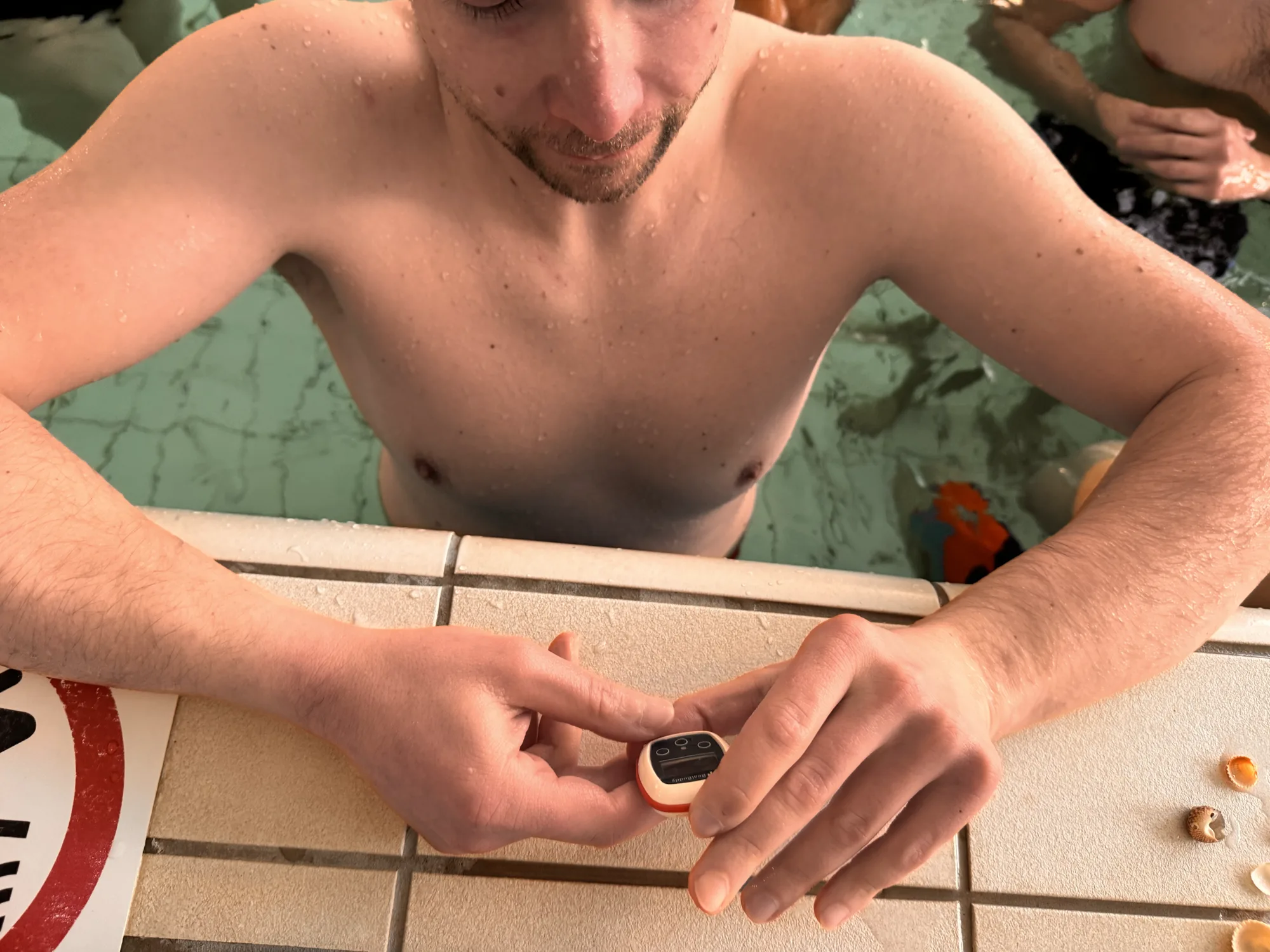 Swimmer resting at the pool wall with a Vimo device on the tiles