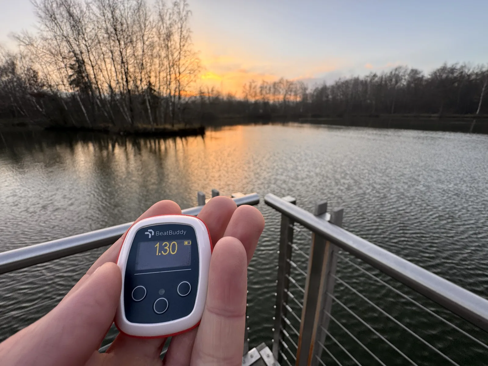 A Vimo tempo trainer set to 1.30 seconds, held in front of an open water swim at sunset