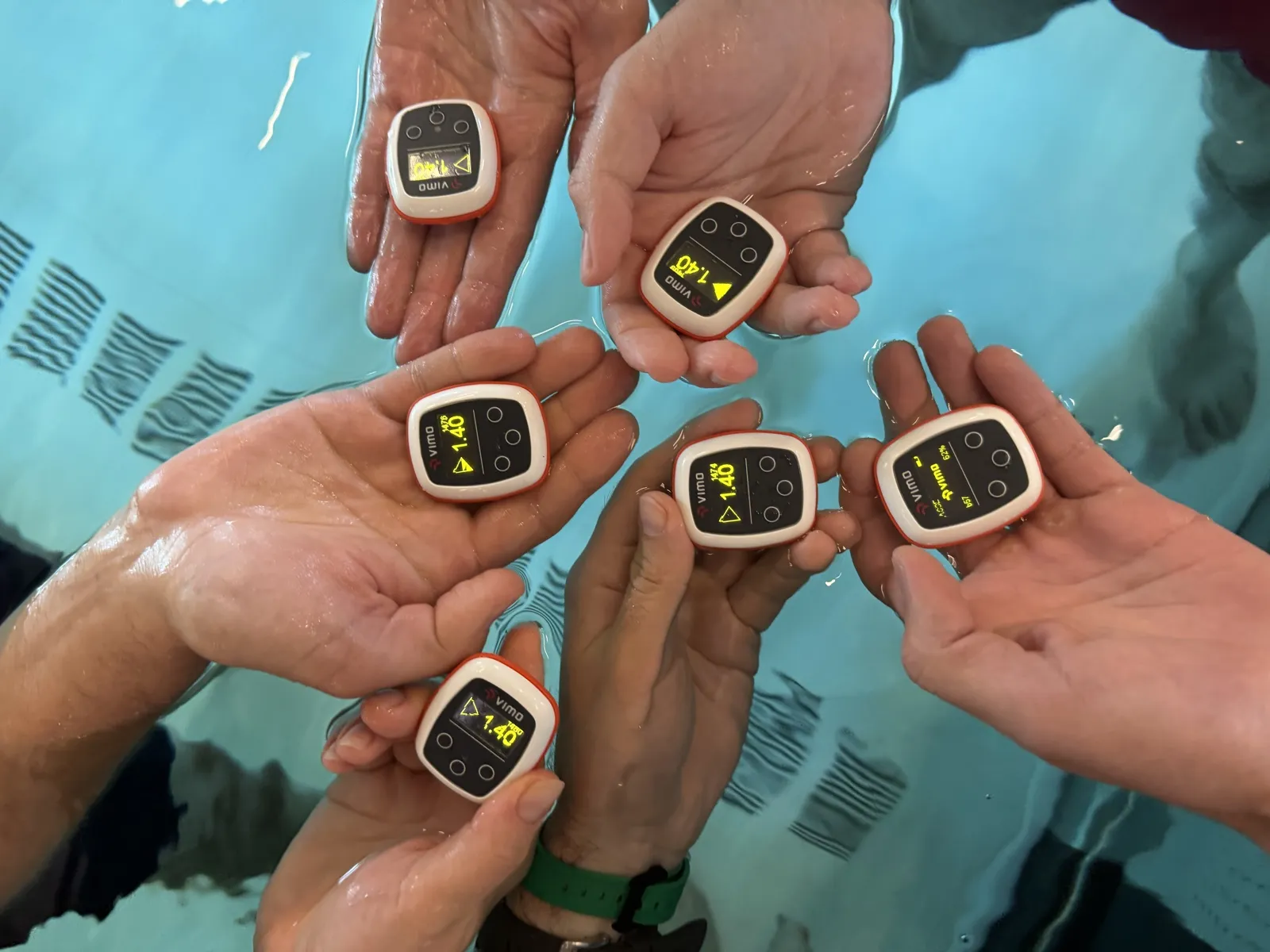 Four hands holding Vimo devices above the water
