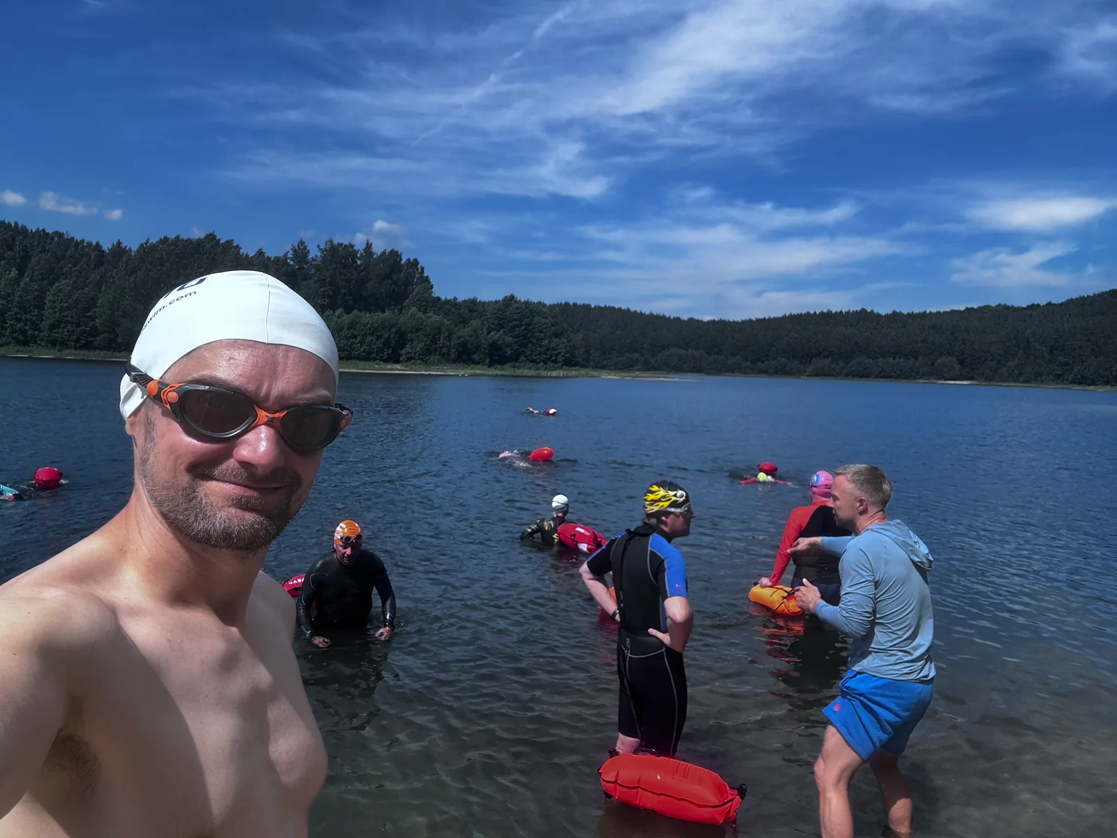 Swimmer in a white cap with an open water group in the lake behind